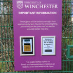 Winchester University Sports Stadium purple and white info sign with snap frames and posters on fence