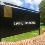 Lainston House black panel and post sign with gold cut-vinyl and white acrylic lettering in field behind wall