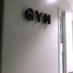 the word GYM in black flat cut acrylic lettering with standoffs on grey door